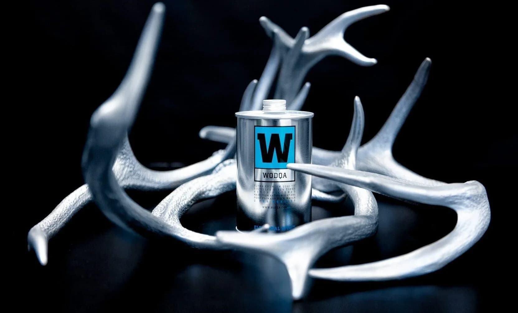 [W]ODQA — radically pure vodka by [X]PLICIT LIQUIDS, a silver can among cast antlers.